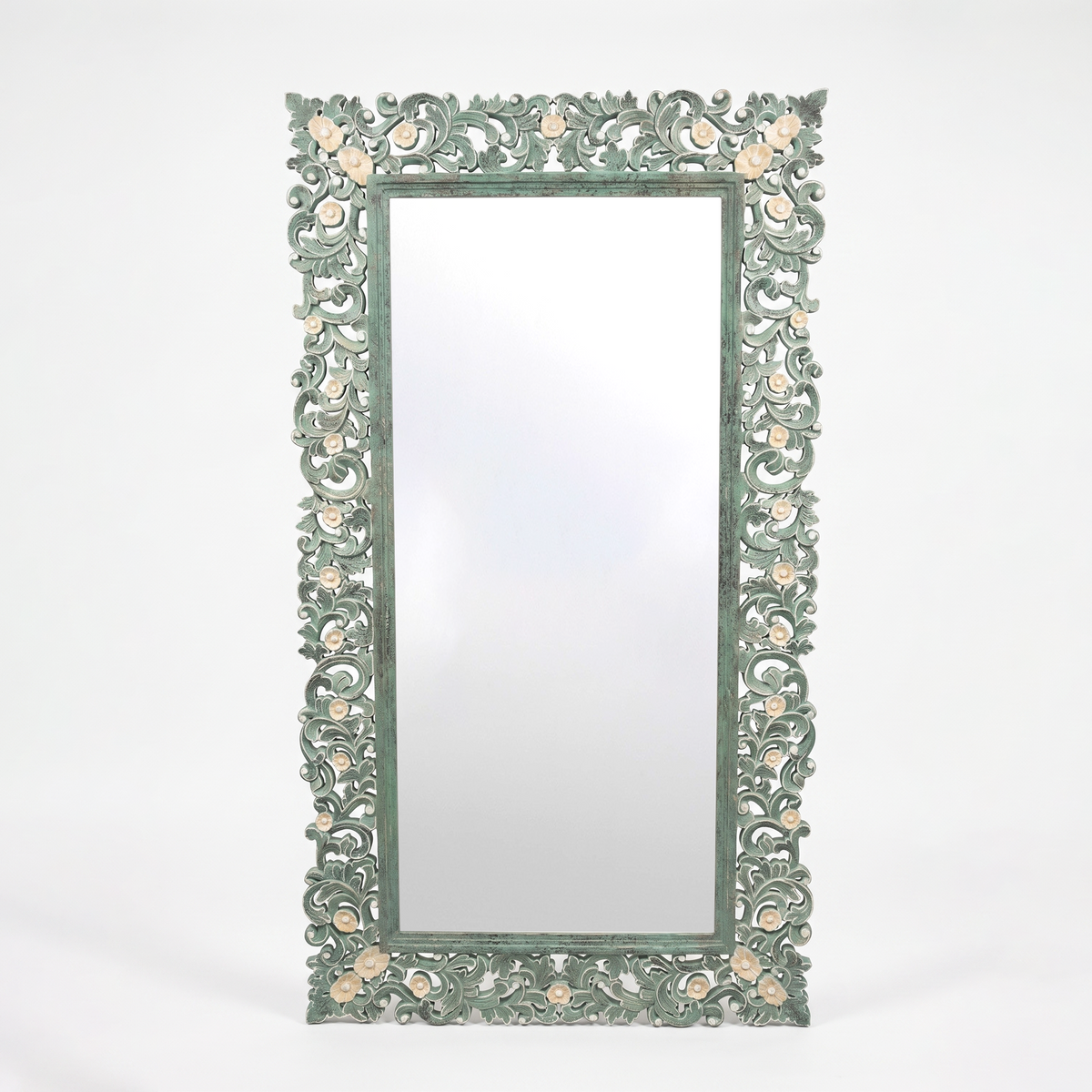 An ornate rectangular wall mirror with a carved, decorative frame in a distressed sage green finish, featuring small peach-colored floral accents, set against a plain white background.